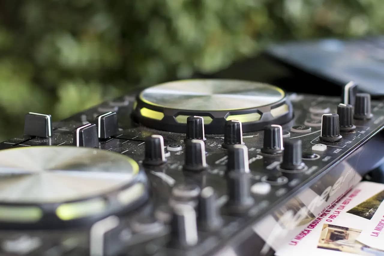 Close-up of a DJ mixer featuring control knobs and platters with a green background.