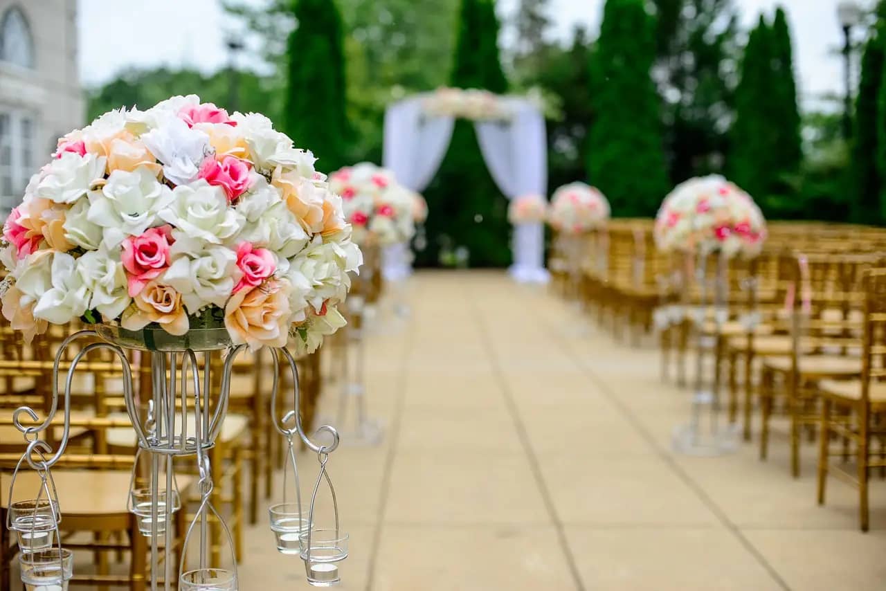 Floral arrangements with pink and white roses on display at an outdoor wedding ceremony.