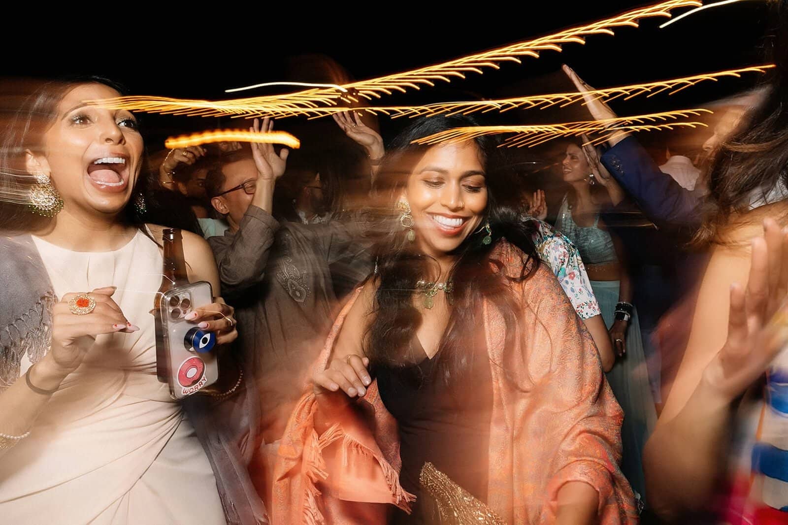 Two women dancing joyfully at a celebration with motion blur effects capturing the energy of the moment.