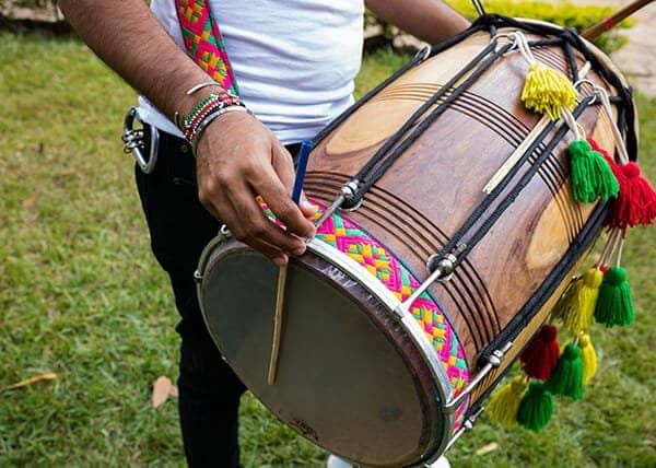 Close-up of a person holding a traditional dhol drum decorated with colorful tassels and a strap.