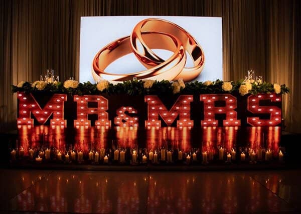 Wedding display featuring a large screen with two gold wedding rings and a decorative MR & MRS sign.